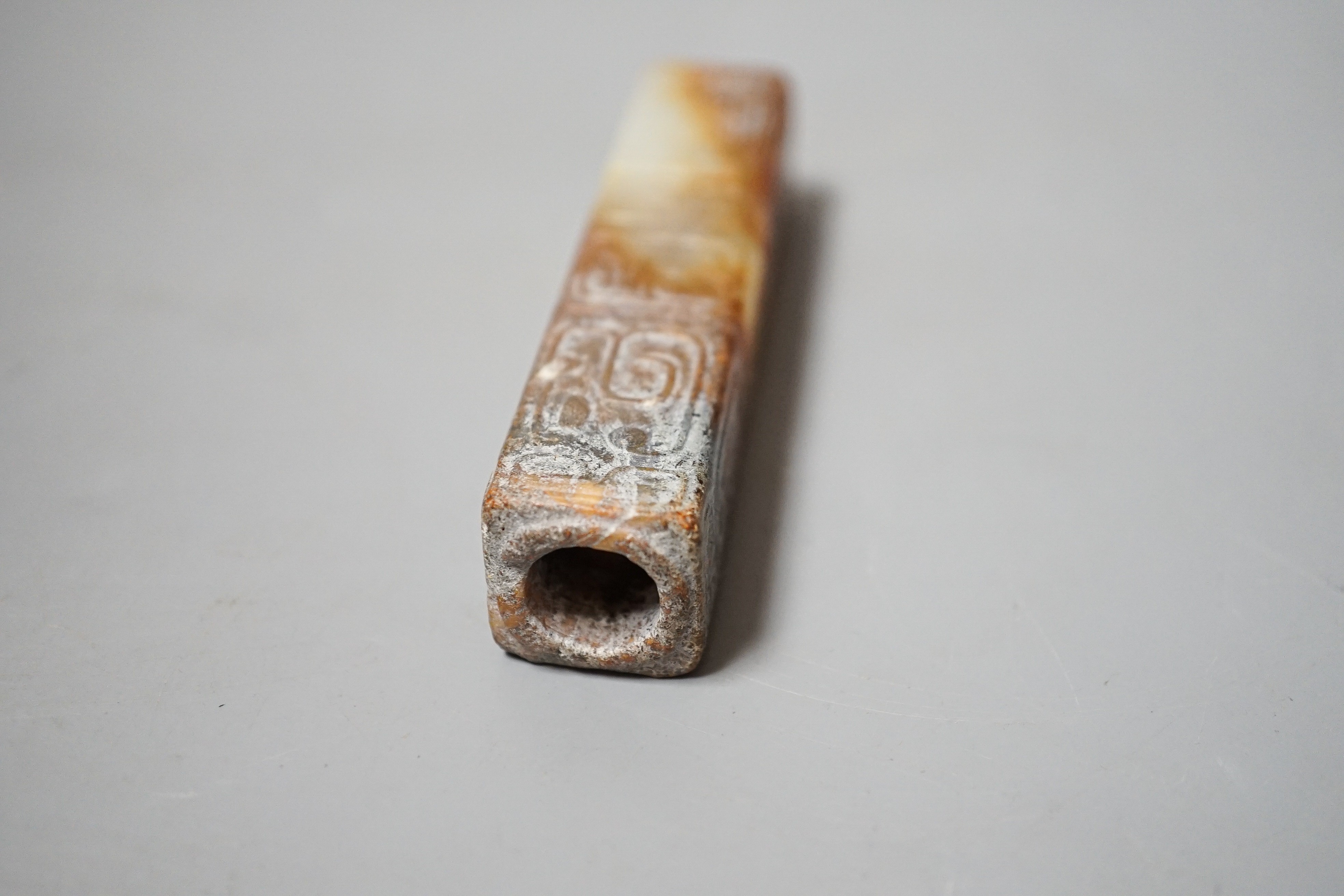 A Chinese archaistic white and russet jade handle mount, carved in relief with three registers of taotie masks, height 9.7cm